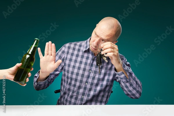 Fototapeta Man refusing alcohol beer showing car key as gesture of don't drink and drive isolated over green background.Do not drink alcohol and drive.