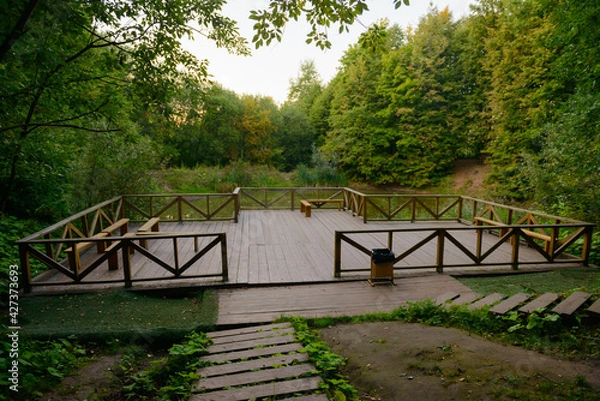 Fototapeta A small observation deck made of wood in the middle of the forest with a pond on a summer evening