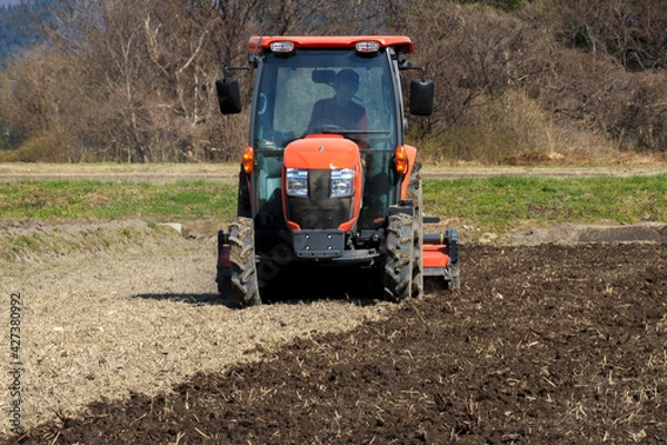 Fototapeta トラクターで田んぼを耕している男性　春　4月　田打ち