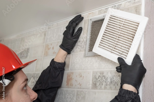 Obraz A professional worker in a protective suit and helmet cleans the Ventilation grill. Flat Panel Fiberglass Filters Of Central Air Condition System With Dust.	
