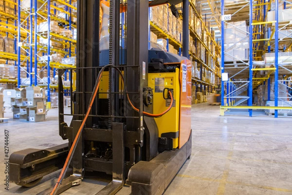 Obraz Electrical forklift loader charging in the warehouse. Pallet stacker truck equipment inside of a modern warehouse storage