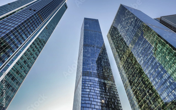 Obraz Three nearby financial centers skyscrapers in one shot. An image from a low angle. The background is a blue and cloudless sky.