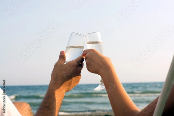 Obraz Two hands holding glasses at the beach