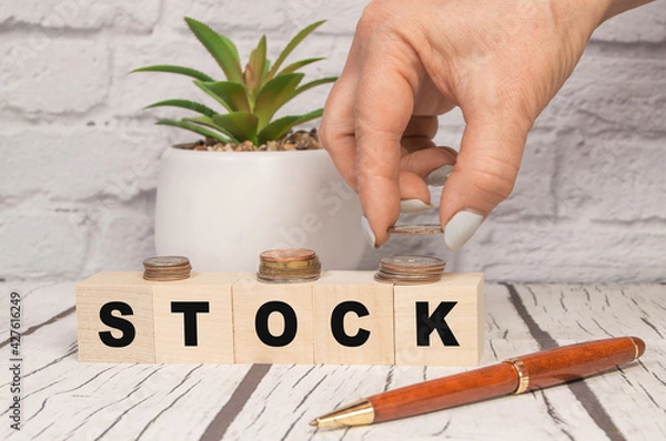 Fototapeta Hand putting coins on stack stair as step growing growth and wooden cube block with word STOCKS. Investment and save money concept