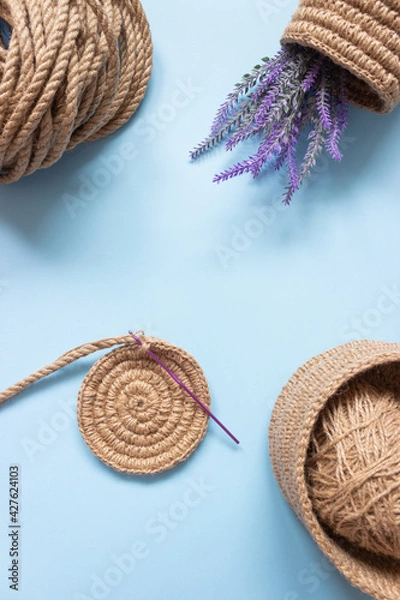 Obraz The knitted part of the basket made of jute rope and a crochet hook. Hobbies, needlework, organization of space.