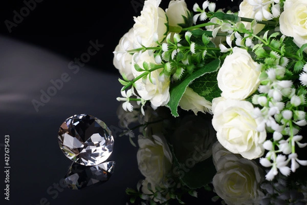 Fototapeta Excellent diamond of the first water and bouquet of white roses with reflection on black mirror background close up view. Jewelry diamonds sale, invitation, action, discount banner, poster template