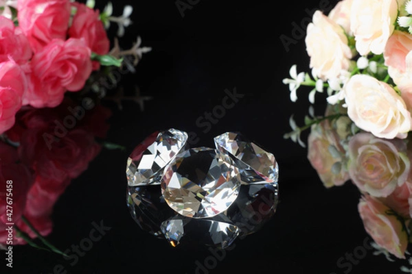 Fototapeta Three excellent diamonds of the first water and bouquets of pink and tea roses with reflection on black mirror background close up view. Jewelry diamonds sale, invitation, discount poster template