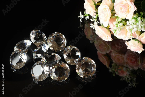 Fototapeta Several excellent pure diamonds and bouquet of tea roses with reflection on black mirror background close up view. Jewelry diamonds sale, invitation, action, discount banner, poster template