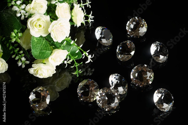 Fototapeta Several excellent pure diamonds and bouquet of white roses with reflection on black mirror background close up view. Jewelry diamonds sale, invitation, action, discount banner, poster template