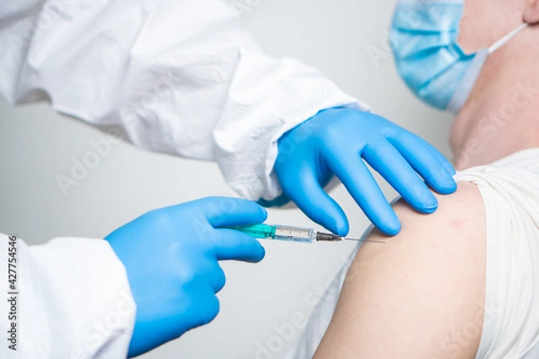 Fototapeta A doctor dressed in a protective suit vaccinates a patient against coronavirus.