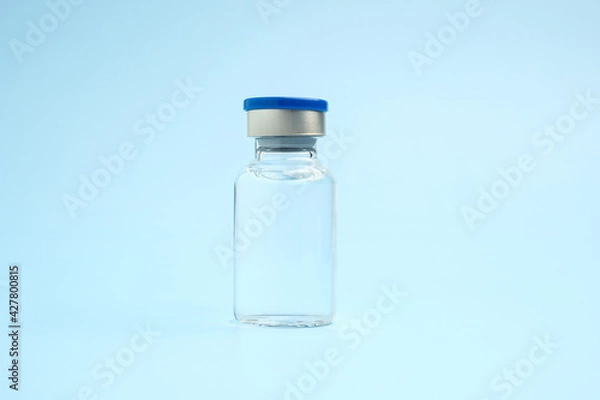 Fototapeta A vaccine in a glass bottle on a light blue background. Vaccine for immunization, and treatment from virus infection. Side view. Concept of medical and healthcare
