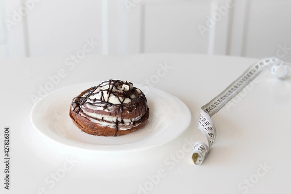 Fototapeta Slimming concept, bun with cream and waist meter