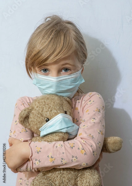 Fototapeta This girl is in a medical mask and holding a teddy bear. The teddy bear is in a mask.