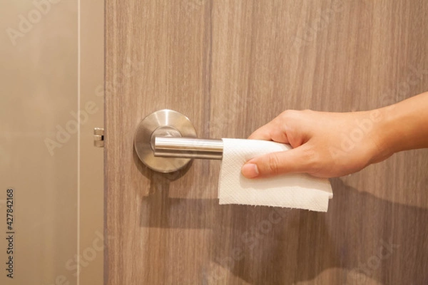 Obraz Closeup of hand opening the public doorknob with tissue paper. Concept of prevent spreading of coronavirus infection.