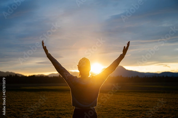 Obraz Woman embracing life standing outside in beautiful meadow with her arms raised high