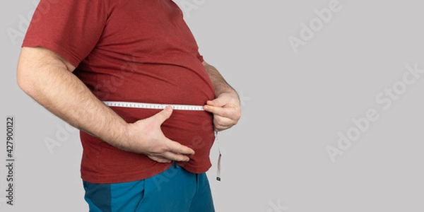 Fototapeta fat man measures the size of the abdomen with a centimeter measuring tape. people suffer from excess weight. banner, copy space