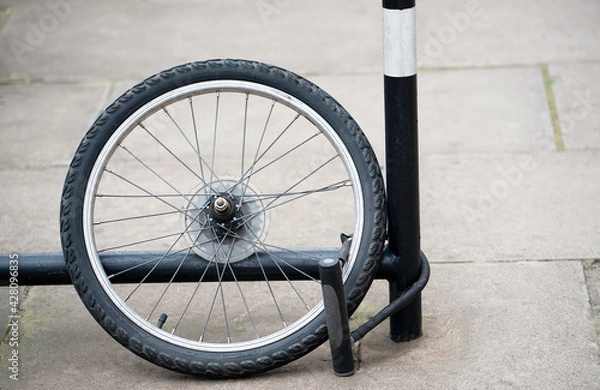Fototapeta Bicycle Theft - Rear wheel of bicycle with lock attached to bike rack. All that remains after the bicycle was stolen.