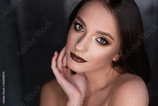 Fototapeta Close up beauty portrait of a brunette girl with brown eyes, professional evening make-up, dark lipstick, smoky eyes in a gold corset. A festive image for a party. Silver dark background. Copy space