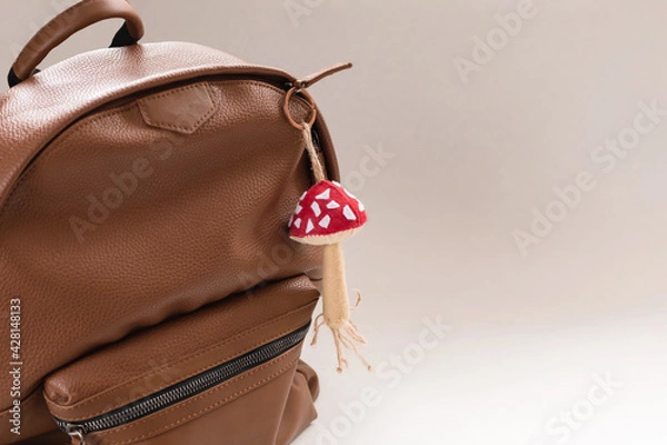 Fototapeta Brown part leather backpack with a mushroom-shaped keychain. The concept of travel, vacation, road, school education.