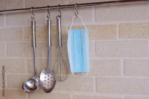 Obraz Kitchen appliances hang on hooks against a white brick wall, and a medical mask hangs among them.