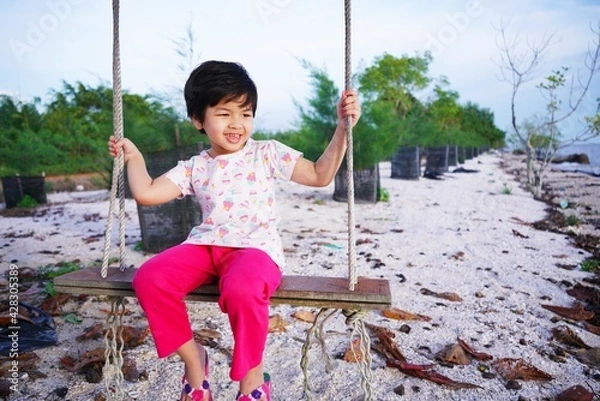 Obraz child swinging on swing.a girl is rocking in a tree on the beach