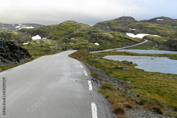 Fototapeta A road leading through the beautiful high plateau mountain area of the Sognefjellsvegen being still covered with snow patches in summer; Norway, Europe