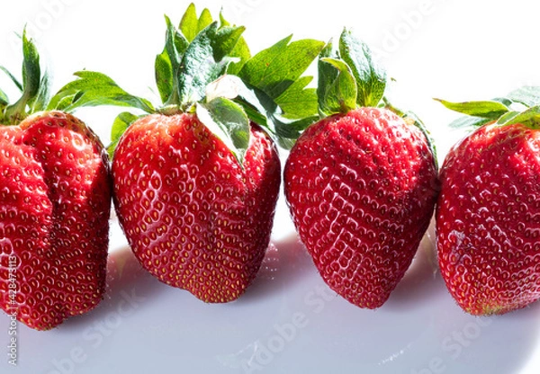 Obraz Detail photo of four very red strawberries with their green leaves on a white methacrylate background.