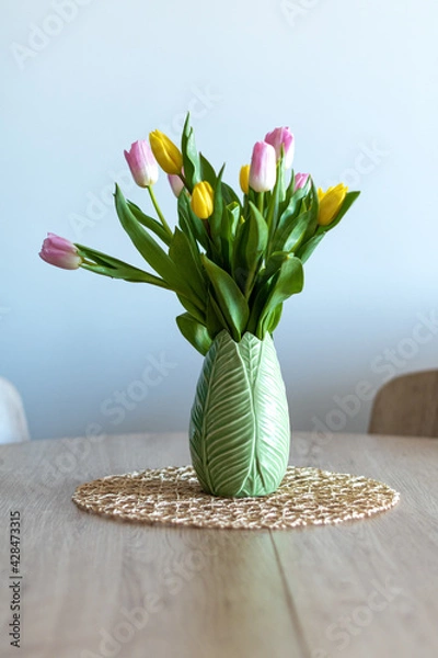 Obraz Vertical photo of a beautiful composition of pink and yellow tulips inside a green vase on a wooden table. White background.