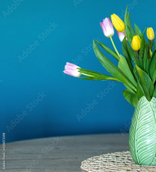 Obraz Vertical photo of pink and yellow tulips inside a green vase inside my house. Composition of half vase. Oil blue background.