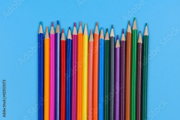 Fototapeta Colored pencils laid out in a row on a blue background.