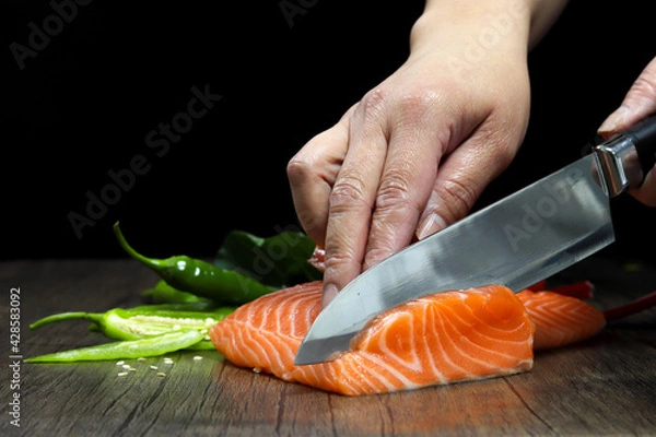 Obraz Salmon is in the hands of the Japanese chef and meticulously done, He is using a knife to slice salmon fillet for sashimi and sushi
