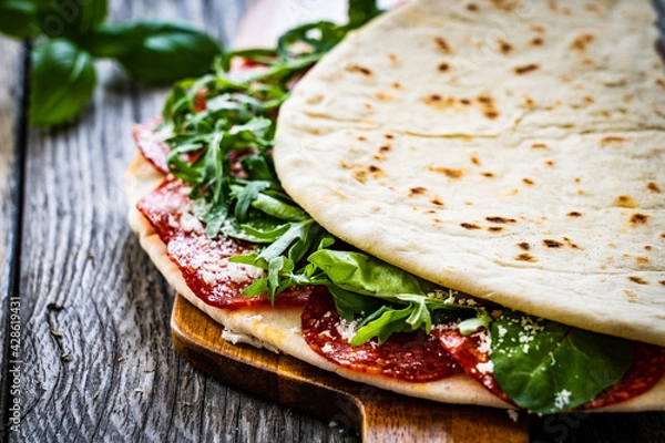 Fototapeta Italian piada wraps - piadina stuffed with fresh vegetable leaves and salami sausage on wooden table
