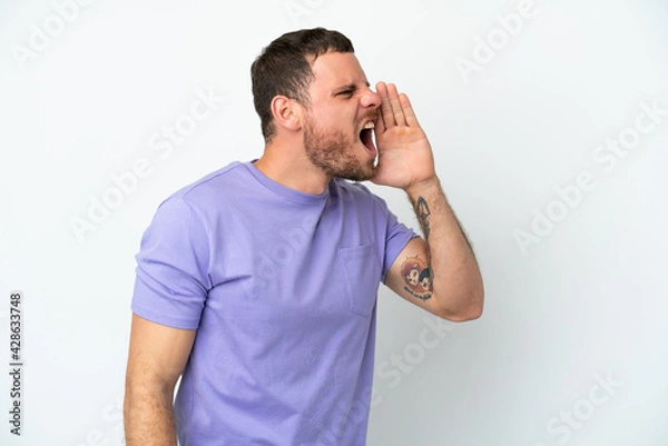Fototapeta Young Brazilian man isolated on white background shouting with mouth wide open to the side