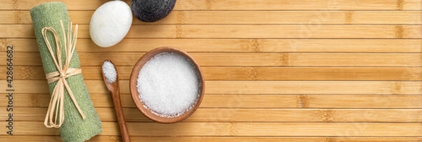 Fototapeta Bath salts natural spa products top view on bamboo wooden texture background with copy space for wellness health concepts. Hot stone massage and exfoliation towel salt in wood bowl.