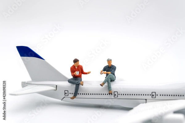 Obraz Travel Concept. Two man miniature figure people with cup of coffee sitting and talking on airplane toy model on white background.