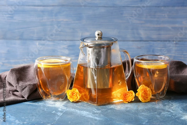 Fototapeta Teapot with hot tea, glasses and flowers on color background