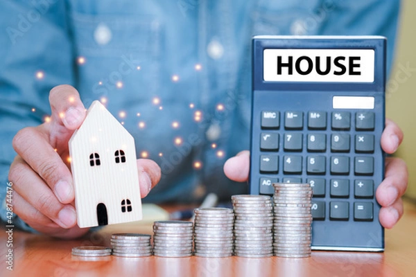 Obraz Both hands were holding a house and a calculator, and coins stacked in front of. The idea of saving money to plan to buy a house in future. Financial calculator.