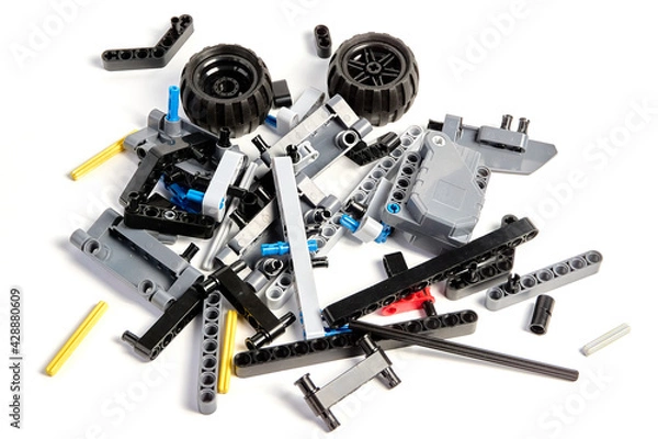 Fototapeta Plastic parts of the constructor, connecting elements and wheels for assembling movable models on a white background, floating focus.