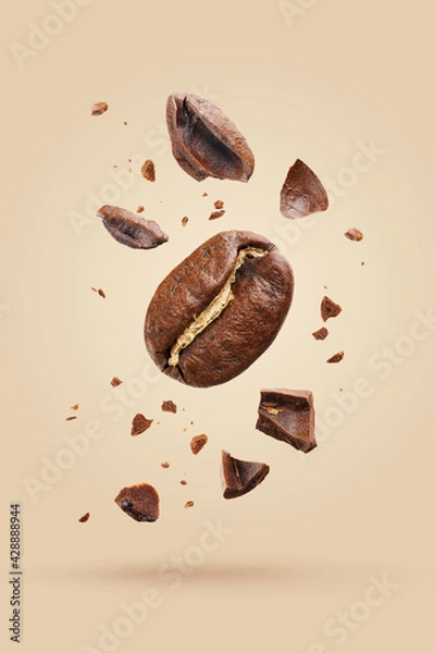 Fototapeta Macro view of roasted beans flying in the air among ground coffee on a beige background. Concepts of levitation. The crash coffee shatters into pieces.