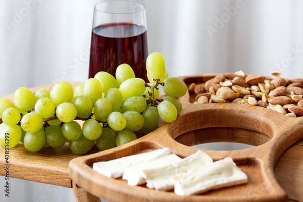 Fototapeta Serving wooden table for wine, glasses and snacks. Handmade segmented Portion wooden table. Grapes, cheese, wine and nuts.  