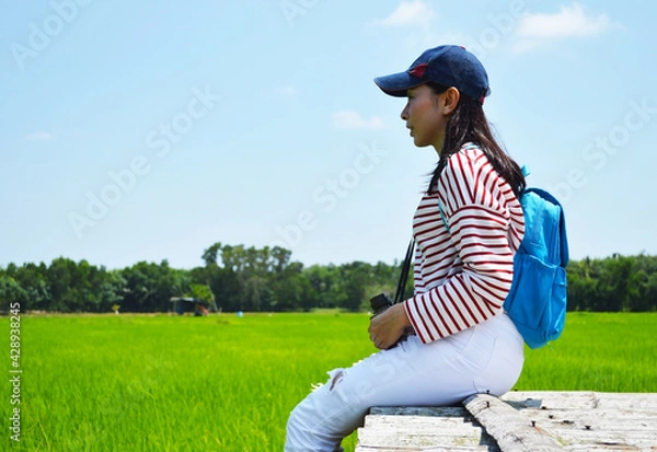 Obraz A woman with a blue backpack sits on a wooden bridge on a clear day.