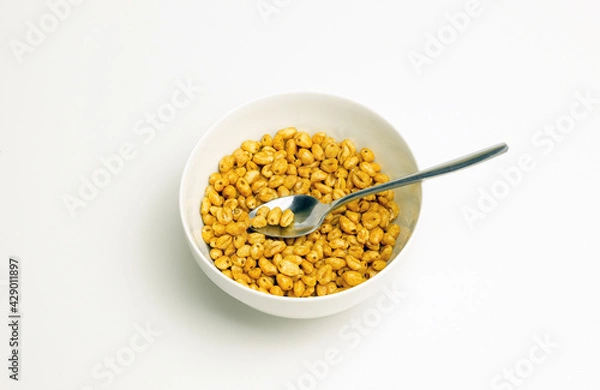 Fototapeta wheat flakes and tablespoon in a white cup on a white background