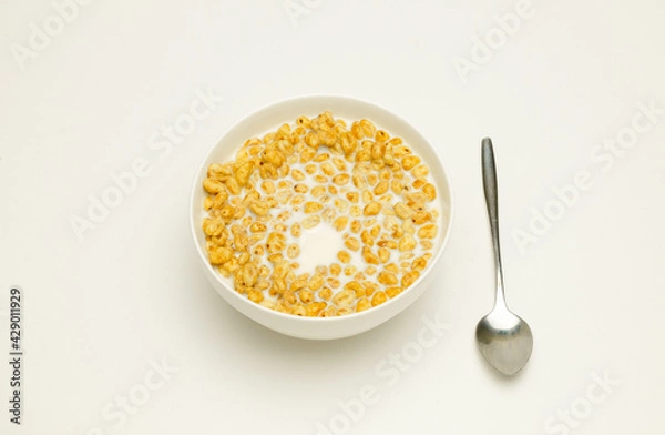 Fototapeta wheat flakes with milk in a white cup and tablespoon on a white background