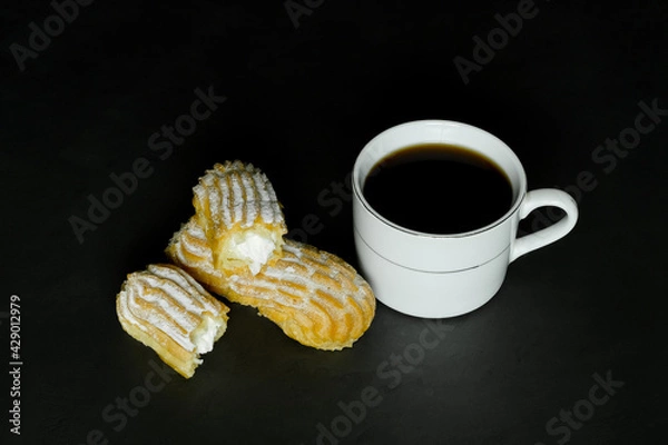 Fototapeta black coffee in a white cup and brewed cakes on a black background