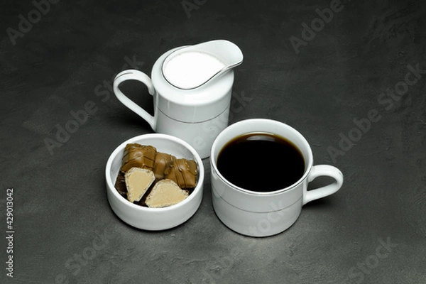 Fototapeta black coffee in a white cup, milk in special dishes and chocolates in a small white saucer on a gray background