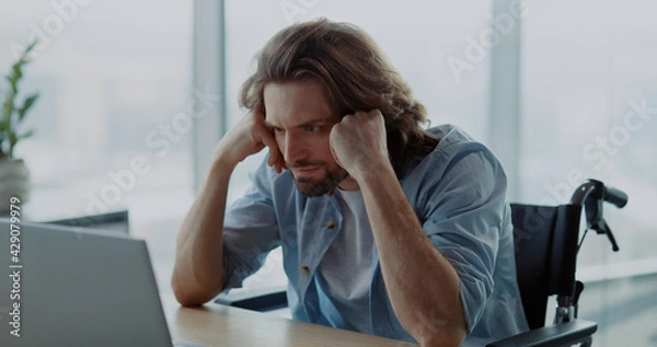 Obraz Young depressed office worker sitting by desk worry about work. Disabled invalid young man frutrating having problems at work.