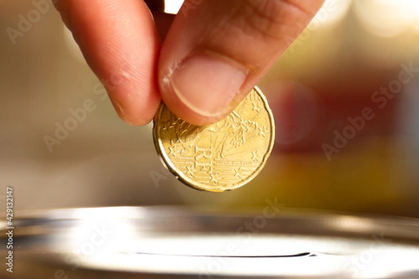 Fototapeta A female hand about to introduce a coin in a money box. Save money concept banner.