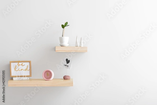 Fototapeta Shelves with alarm clock and decor on white wall