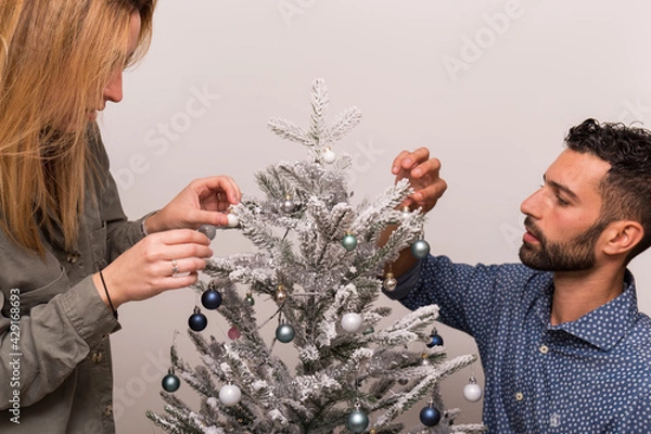 Obraz couple decorating a Christmas tree, young couple decorating a small Christmas tree with blue and silver balls