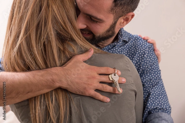 Obraz Young couple hug each other very happy because they have just bought a house, the man has the keys to his new house in his hand and hugs his wife who is on her back
